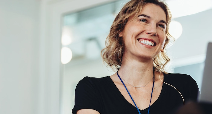 Blonde vrouw lachend op kantoor met een headset en een laptop in beeld.