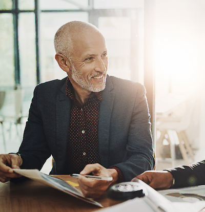 Zakelijke man in pak die glimlachend over een document praat tijdens een vergadering.