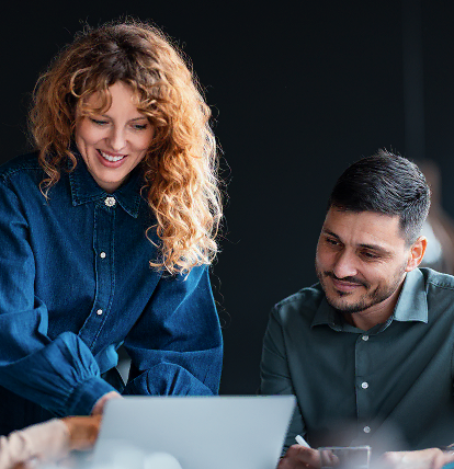 Twee collega’s werken met een glimlach samen aan een laptop.