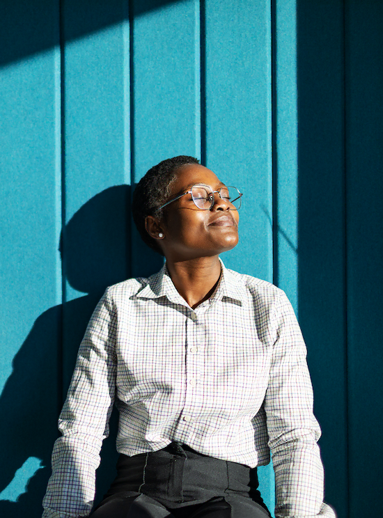 Vrouw geniet binnen van zonlicht tegen een felblauwe muur.