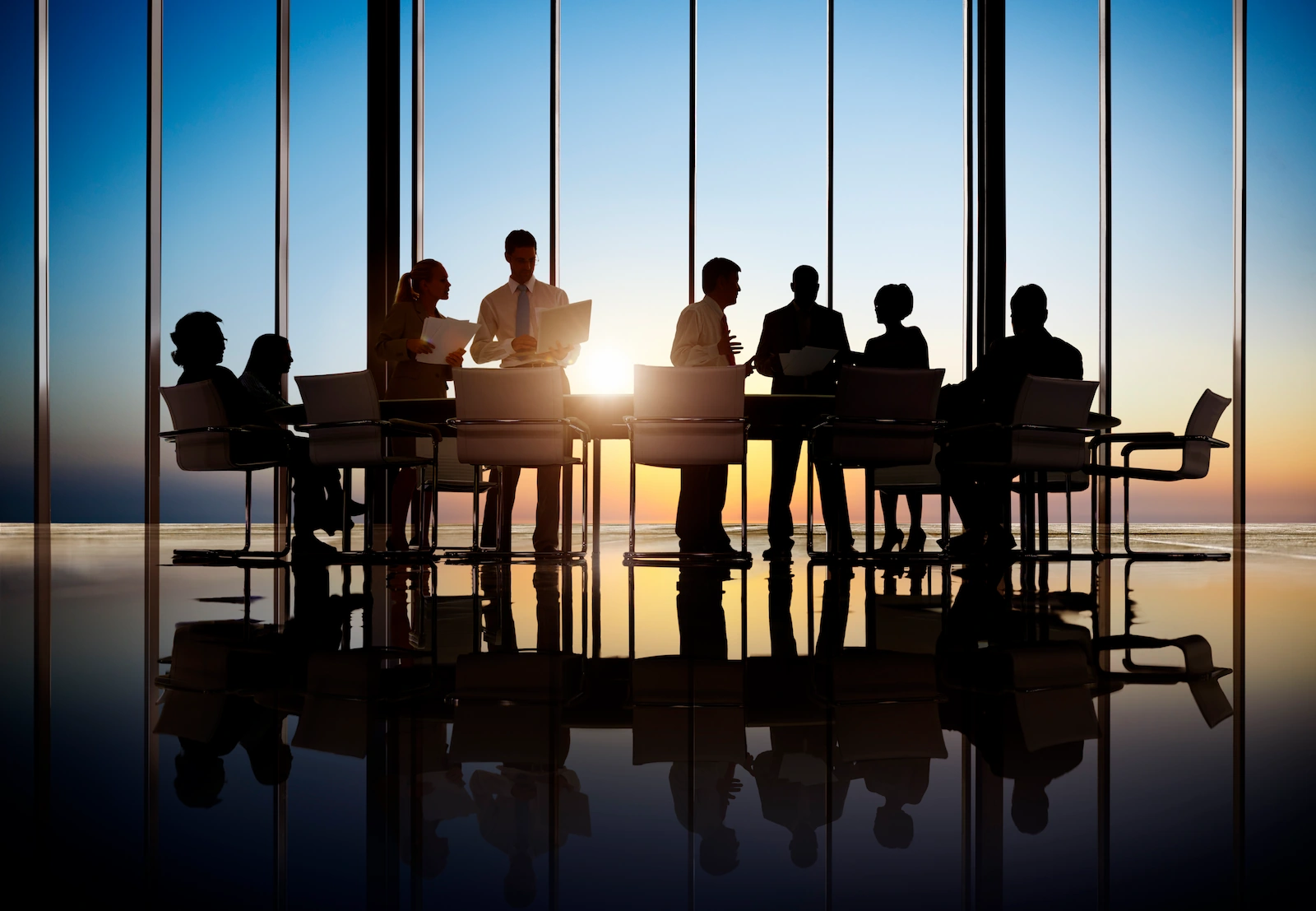 Een groep mensen werkt samen in een vergaderruimte met grote ramen tijdens zonsondergang.